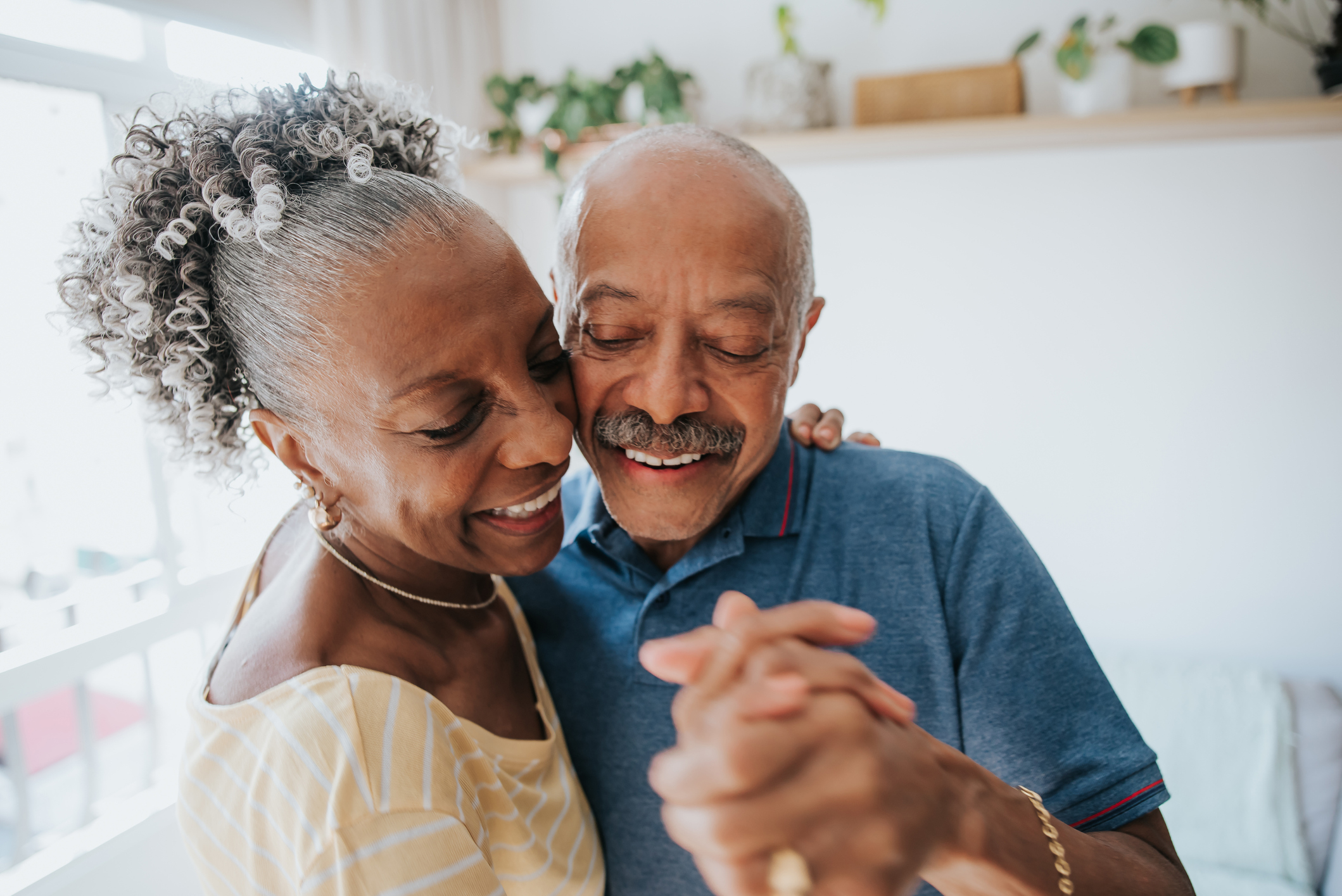 An older couple is dancing in the kitchen together