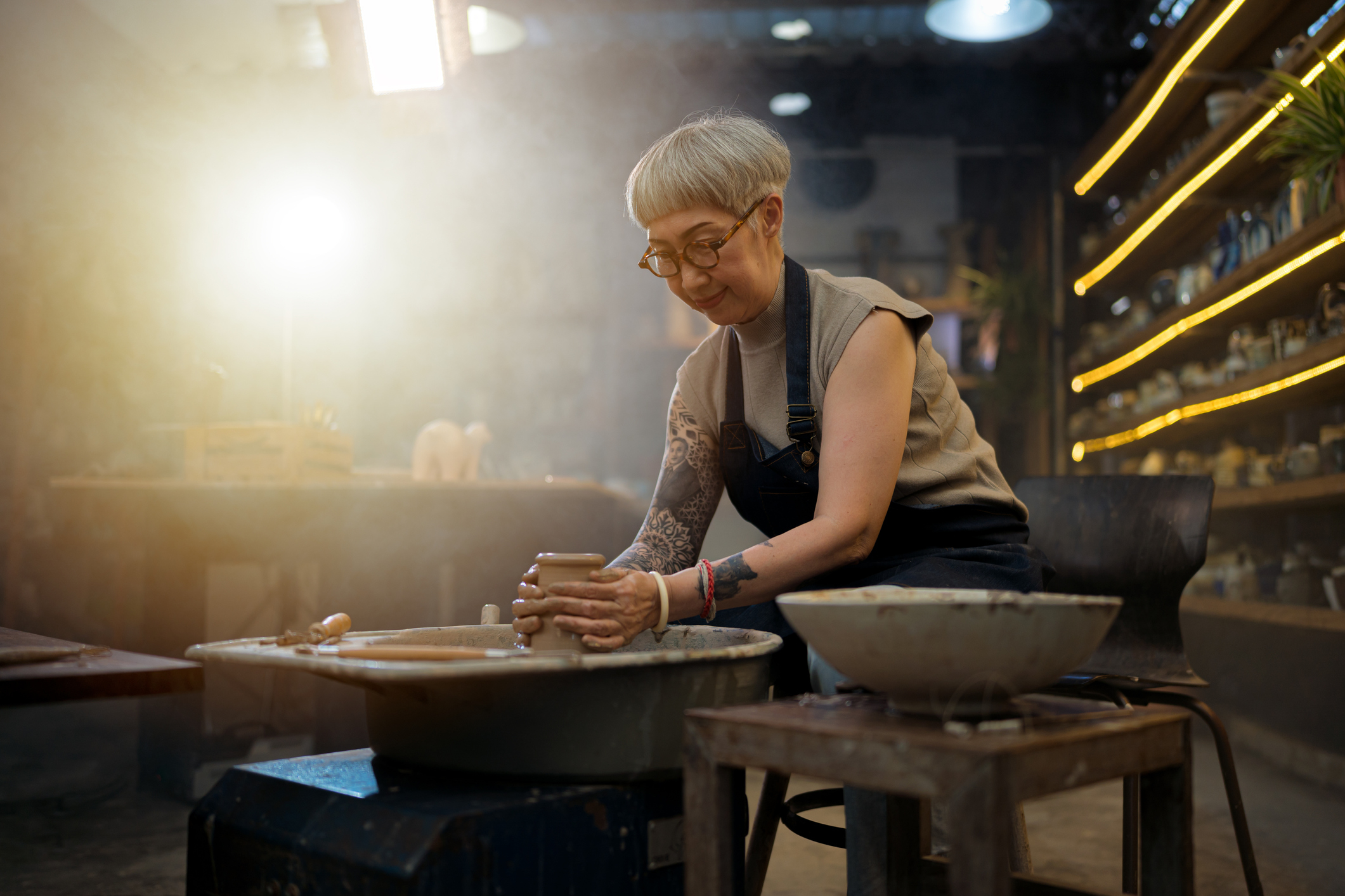 A tatted-up older woman is doing pottery