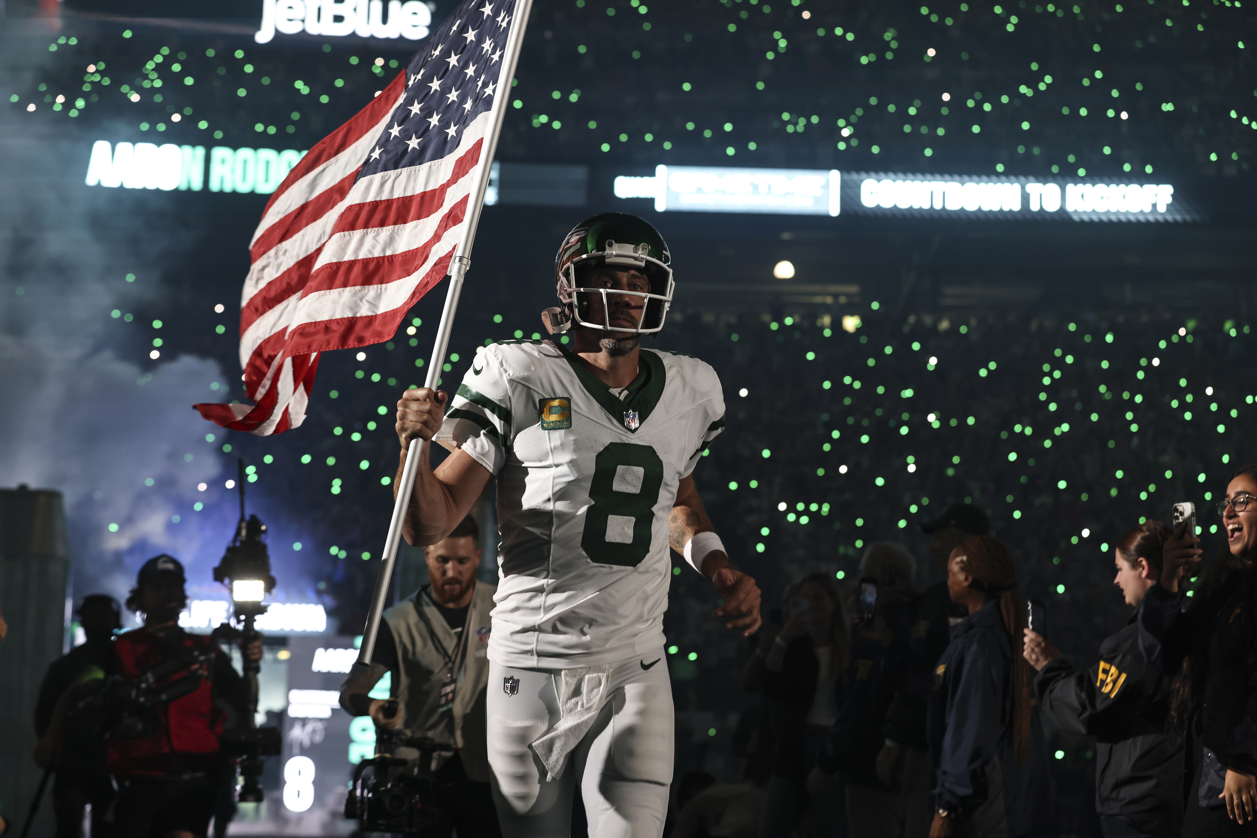 Aaron Rodgers #8 of the New York Jets takes the field holding an American flag
