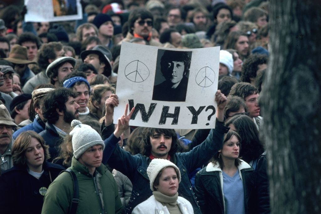 crowd outside after john&#x27;s death, someone holding a sign with his photo and why? written out