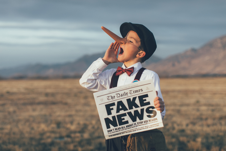 kid holding a newspaper with the headline, fake news