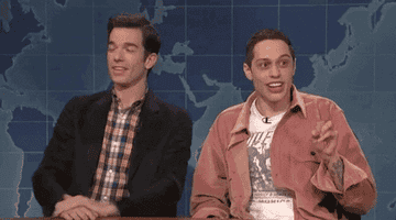 John Mulaney and Pete Davidson sit side by side as Pete shouts "TWO" holding up two fingers.