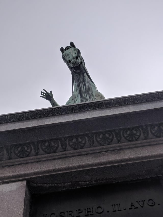 statue of a horse creeping from the side of the building that looks like it&#x27;s waving with a human hand