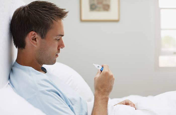 Man looks at thermometer in bed