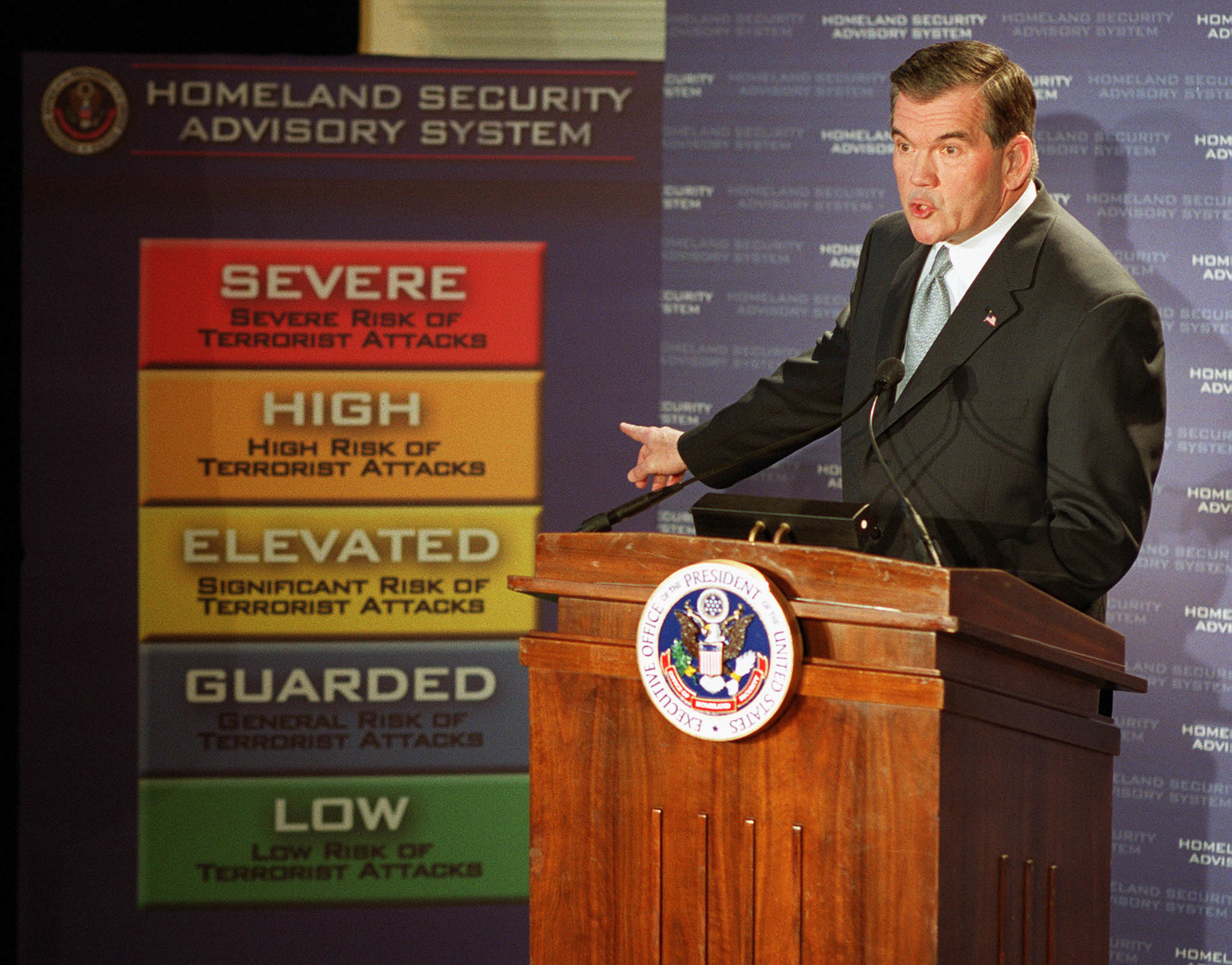 man at a podium pointing to the color coded sign