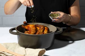 Person adding spices to a roasted chicken in a Goodful Charcoal Dutch Oven