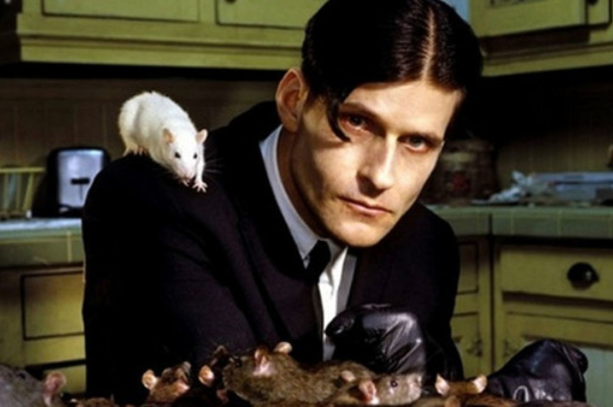 Man in suit with gloved hands, surrounded by rats and one on his shoulder