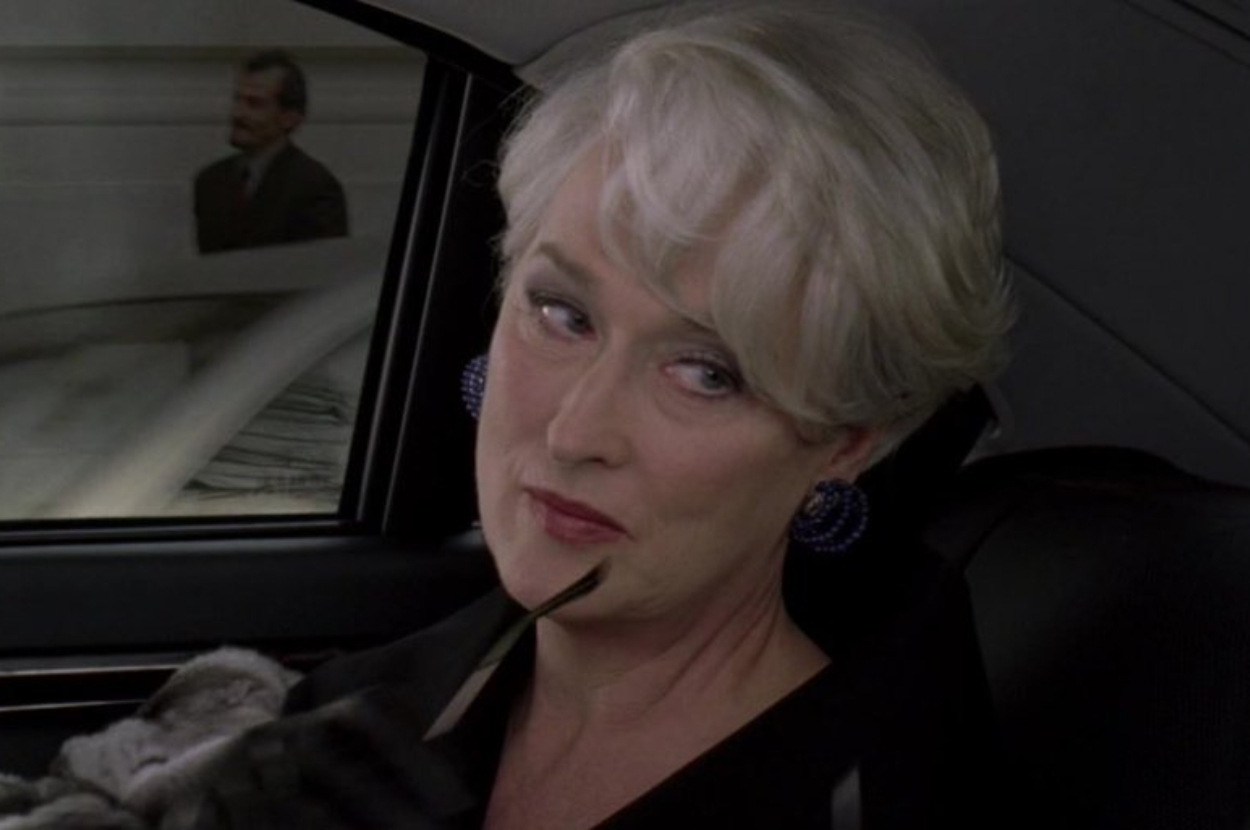 Miranda Priestly from The Devil Wears Prada wearing a coat and earrings, holding sunglasses in a car