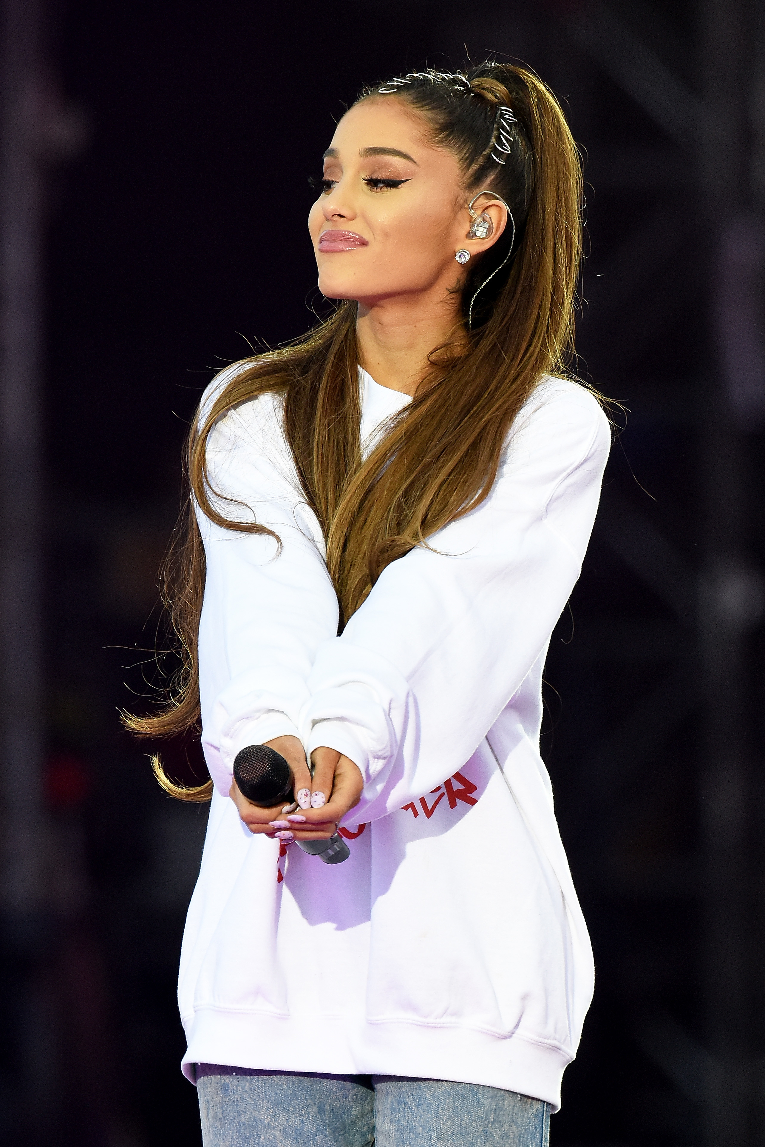 Close-up of Ariana holding a microphone and wearing an oversize sweatshirt and jeans