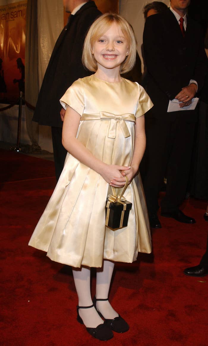 Smiling Dakota in a dress and small gift box handbag on the red carpet