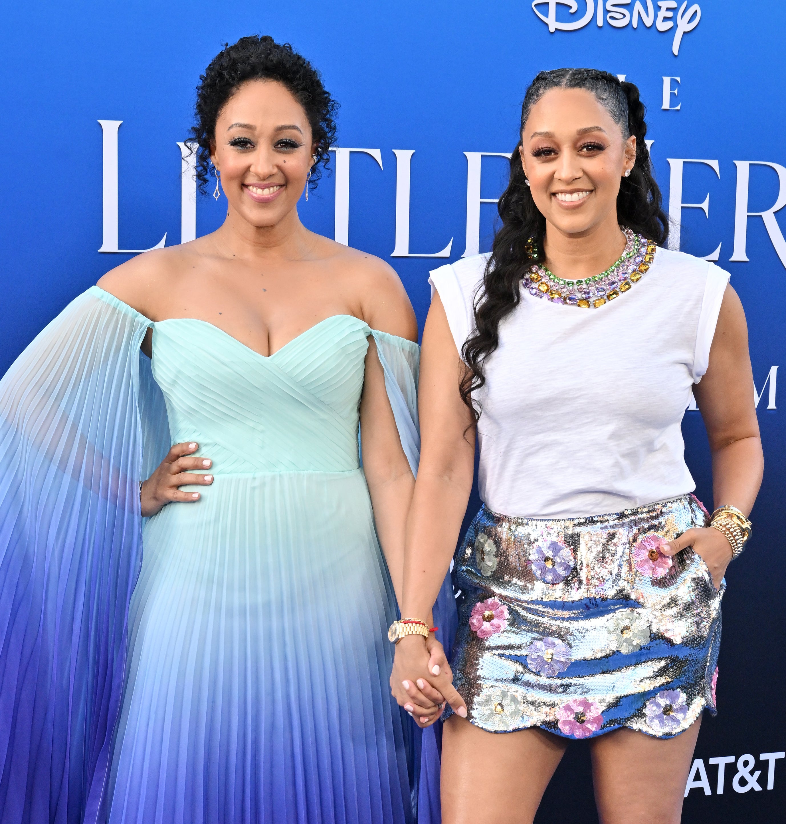 The smiling sisters holding hands, with one wearing a gown and one wearing a miniskirt