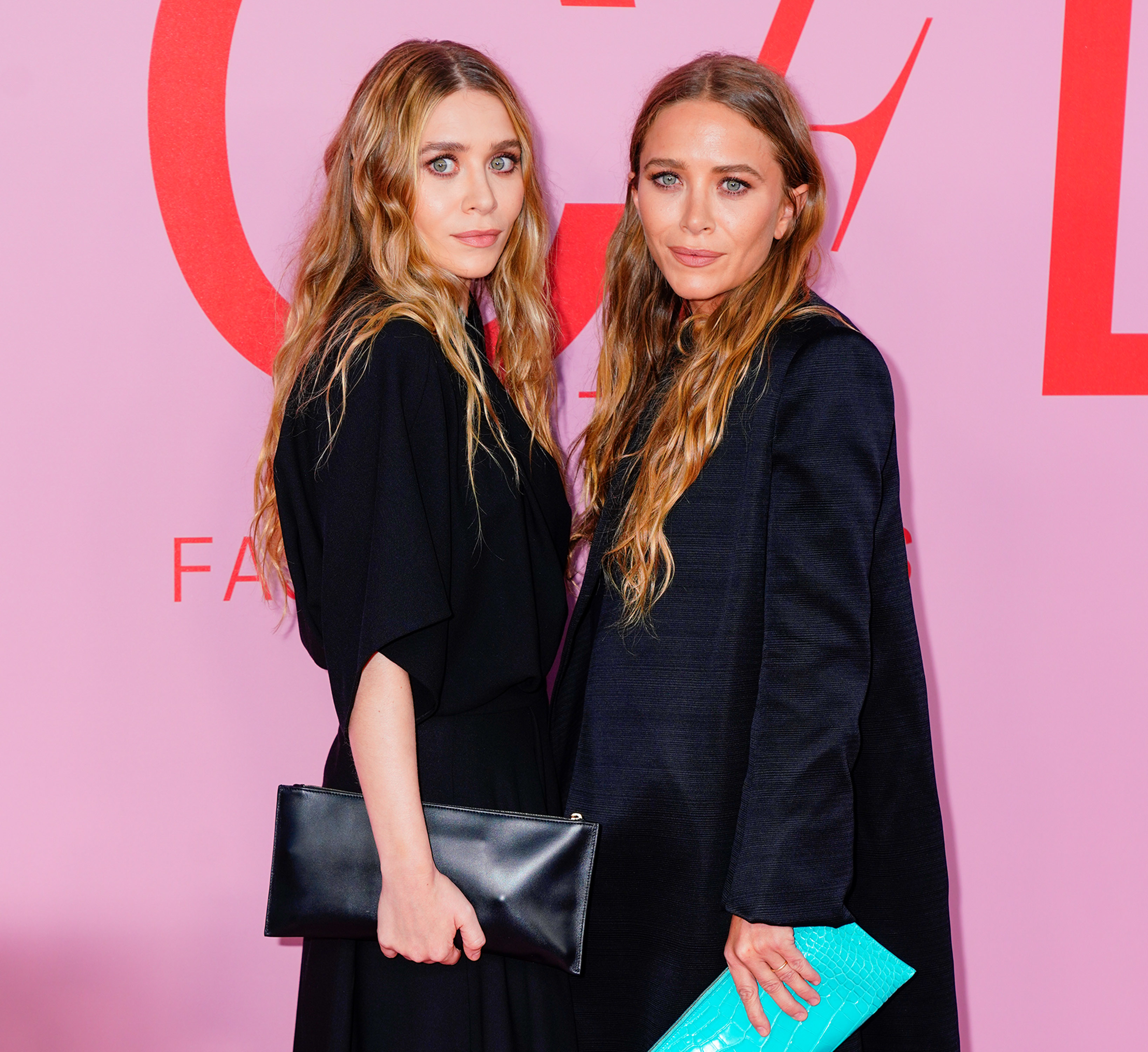 Mary-Kate and Ashley facing each other and holding purses and wearing dark outfits
