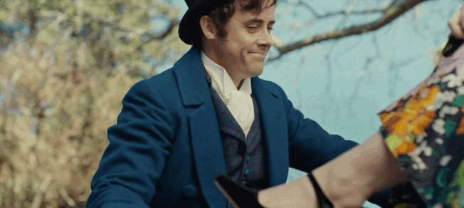 Man in 19th-century attire and top hat, smiling, helping someone adjust their shoe