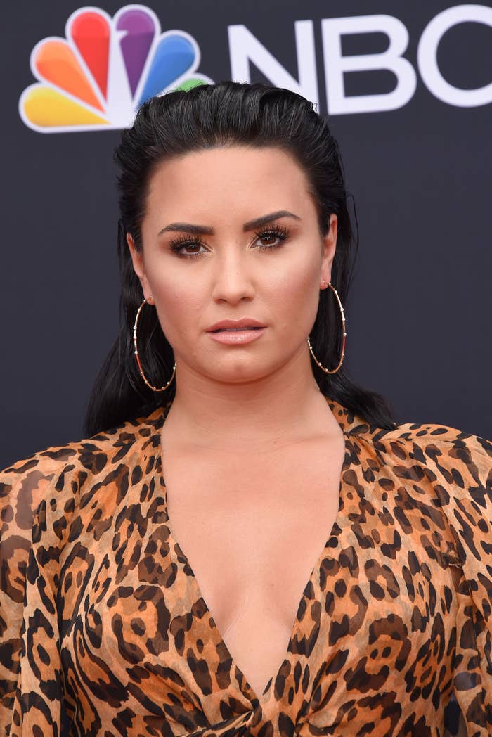 Close-up of Demi at a media event, wearing a deep-V animal-print top