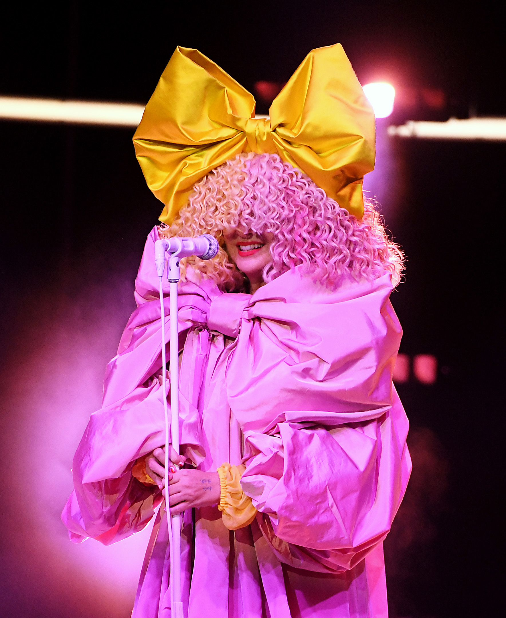 sia performing on stage in an oversized dress and large wig covering half her face