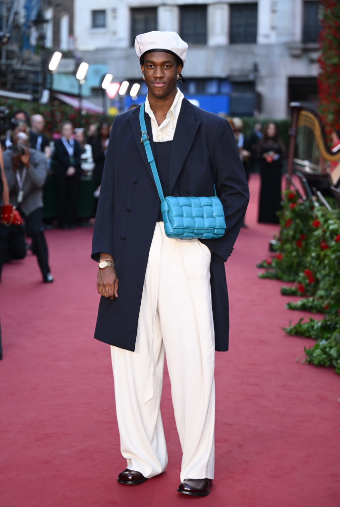 wearing baggy pants and a long coat over a button-down with a purse