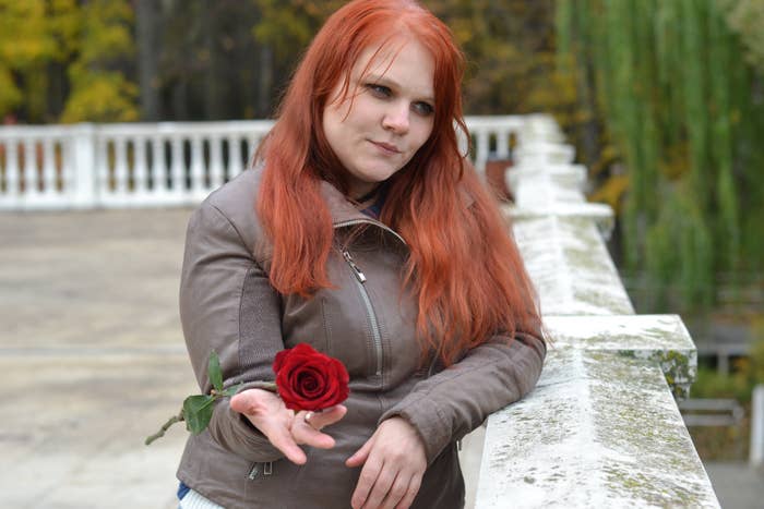 A woman standing on a balcony looking forlorn while holding a single rose