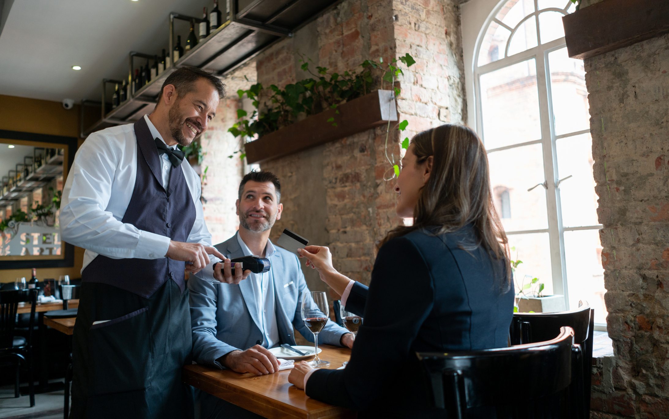 A woman sitting with a man and giving the waiter a credit card