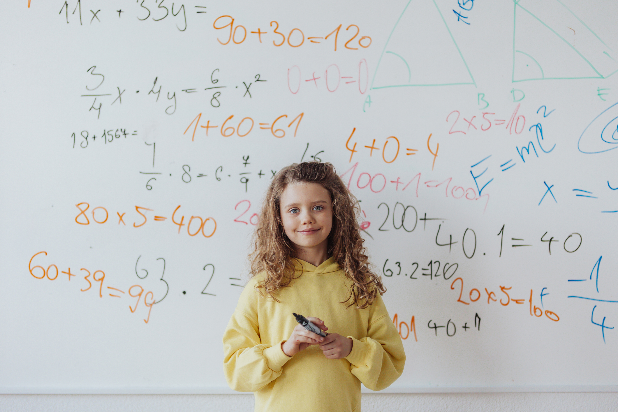 a little girl stands smiling in front of a whiteboard filled with math equations