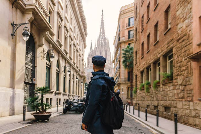 A person with a backpack on a narrow European street looking at a cathedral