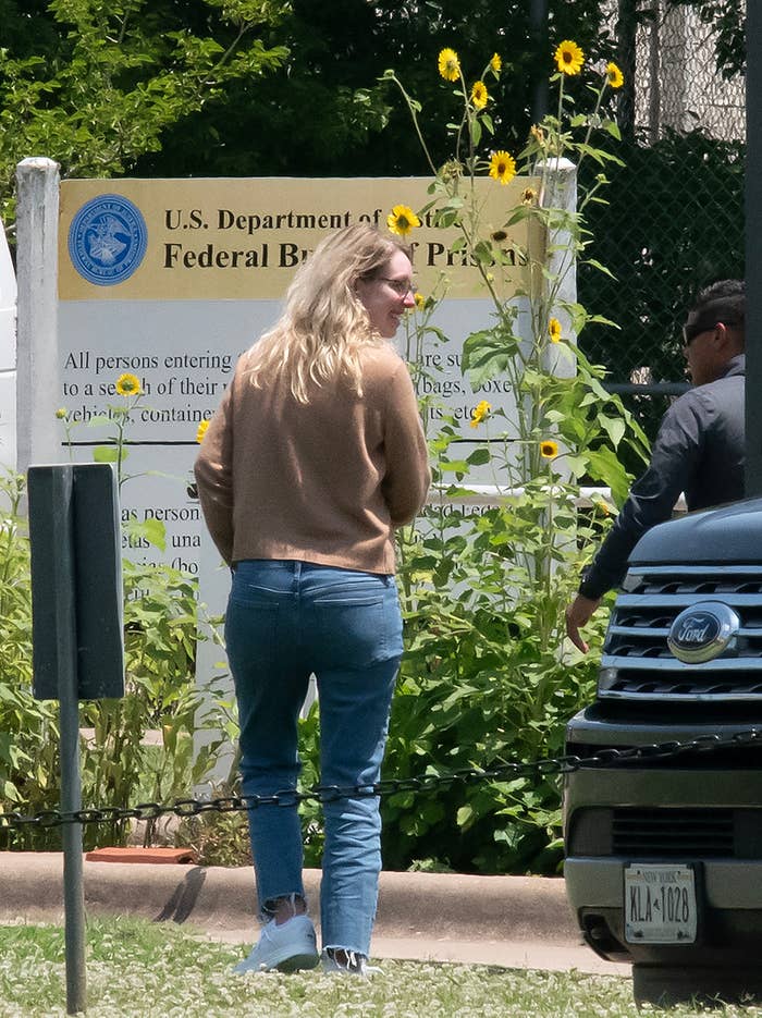 Elizabeth smiling and wearing jeans in front of a &quot;US Department of Justice Federal Bureau of Prisons&quot; sign