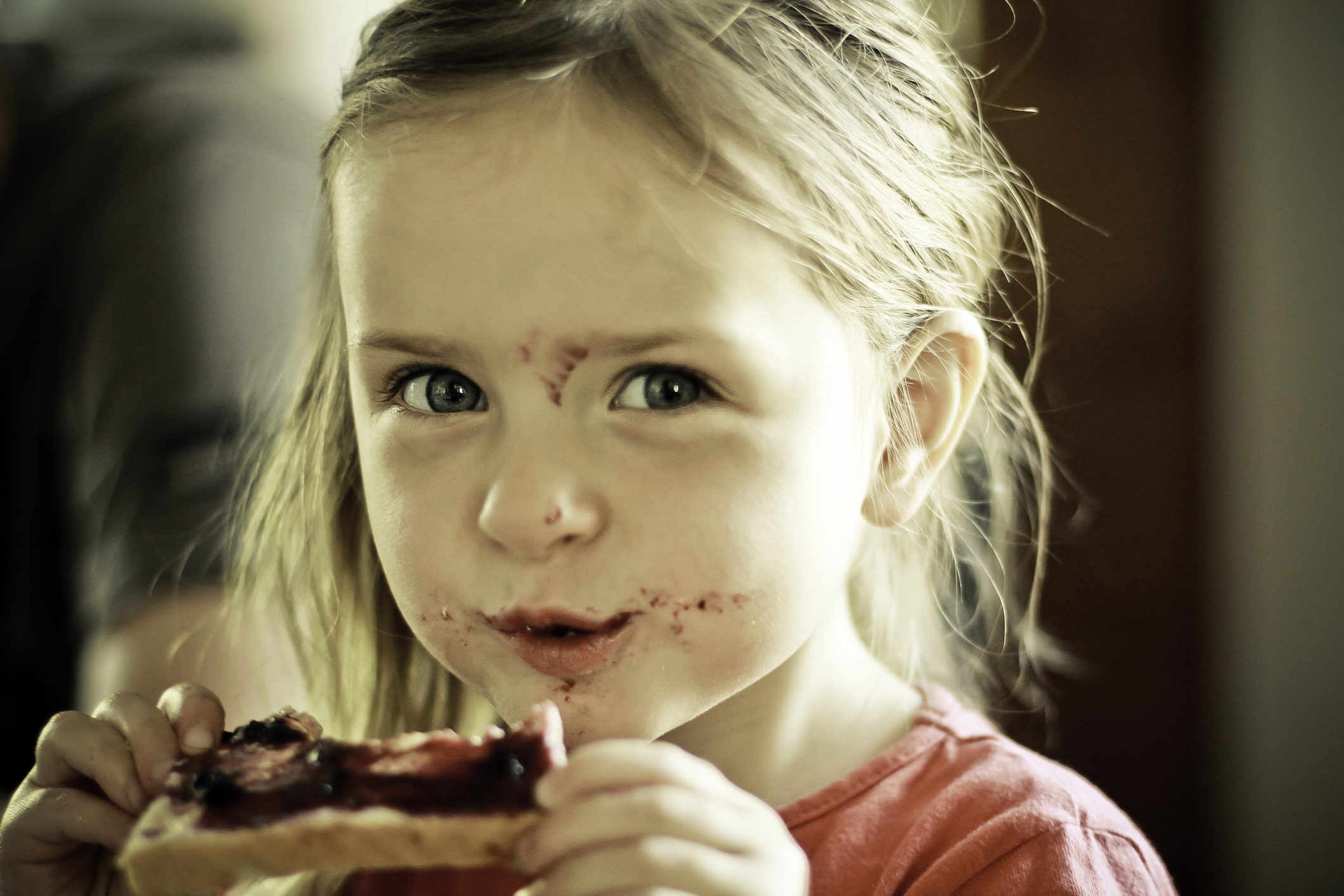 Child eating a PB&amp;amp;J sandwich with jelly on their face