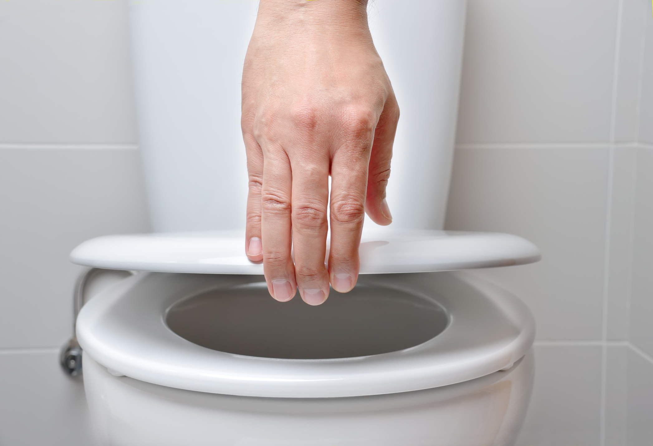 A hand closing a toilet lid