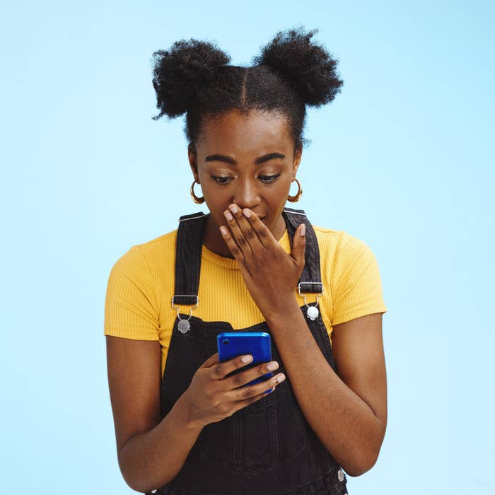A woman looking at a cellphone and covering her mouth in shocke