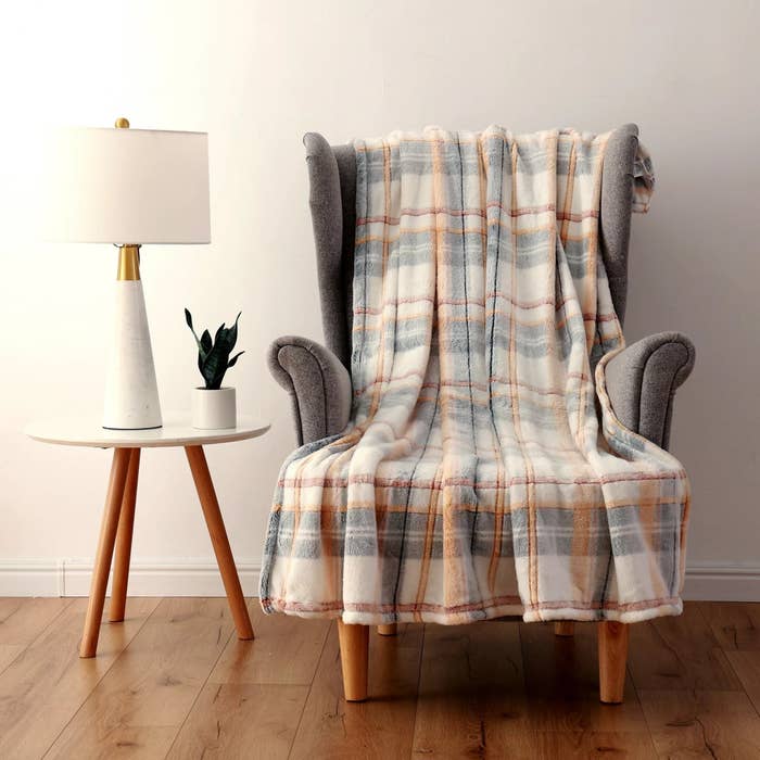 The plaid blanket in muted colors, draped over a chair to show its soft texture