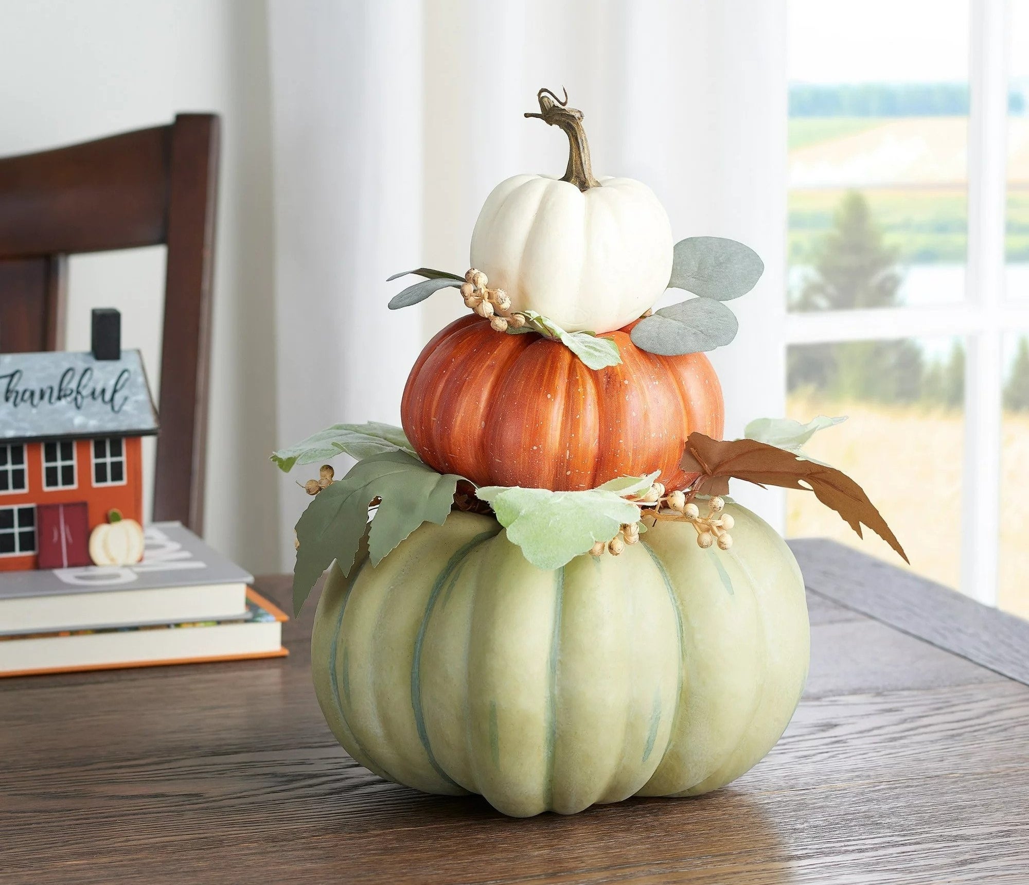 Three pumpkins stacked from smallest to largest in white, orange, and green respectively