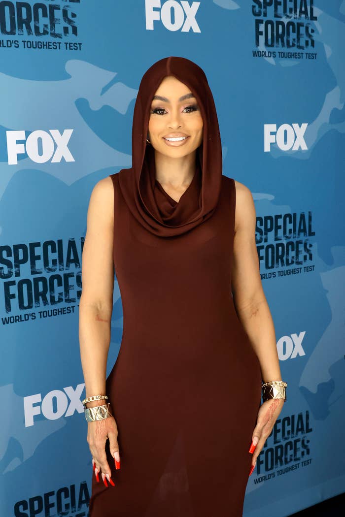 Blac Chyna smiling at a media event in a sleeveless cowl-neck and hood outfit