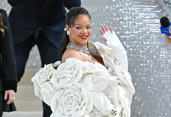 Rihanna waving to fans as she walks a red carpet in a voluminous gown with rosettes