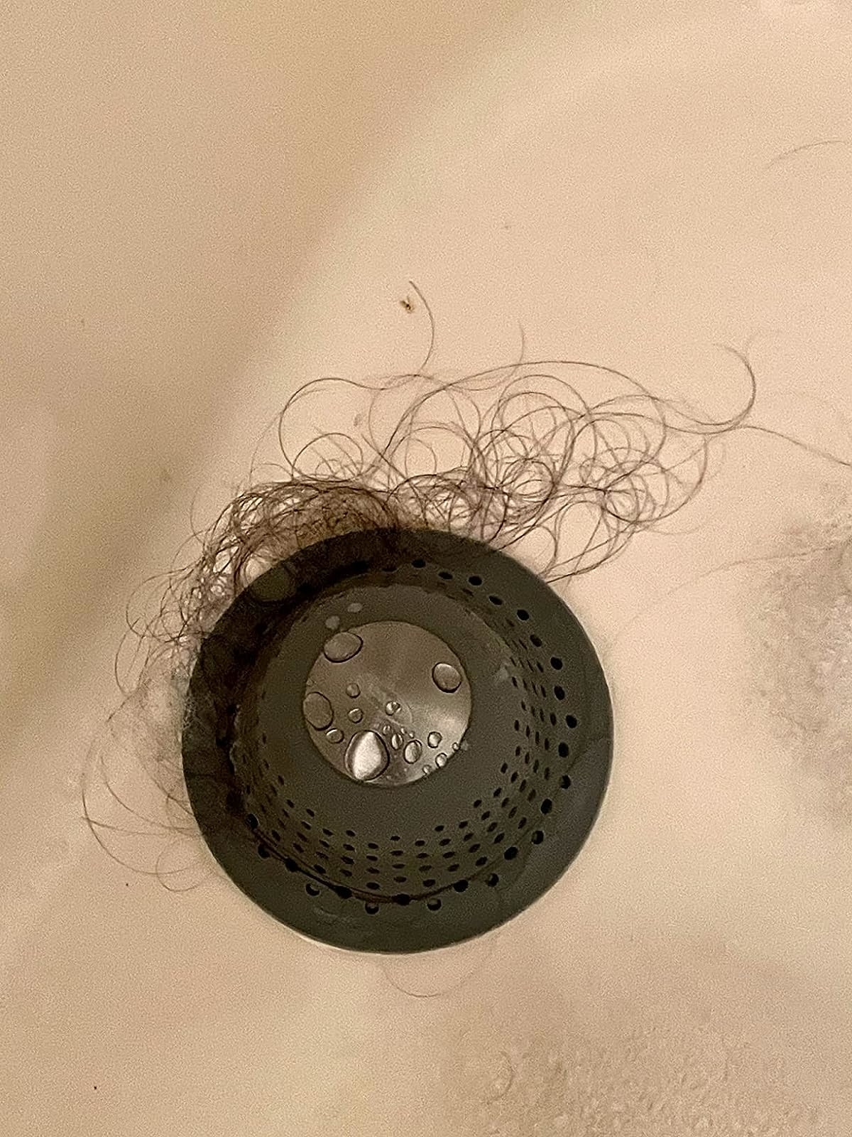 Reviewer&#x27;s photo of the drain cover in a tub, catching lots of hair