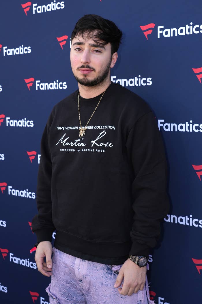 Zack Bia stands on the red carpet of a media event wearing sweater and jeans