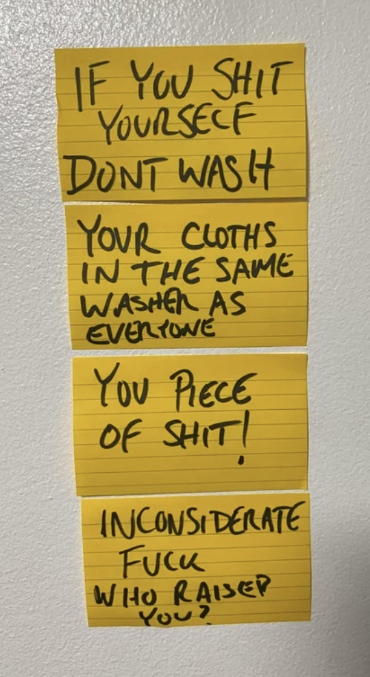 A series of Post-It notes on the wall say "if you shit yourself, don't wash your clothes in the same washer as everyone else, you piece of shit. Who raised you?"
