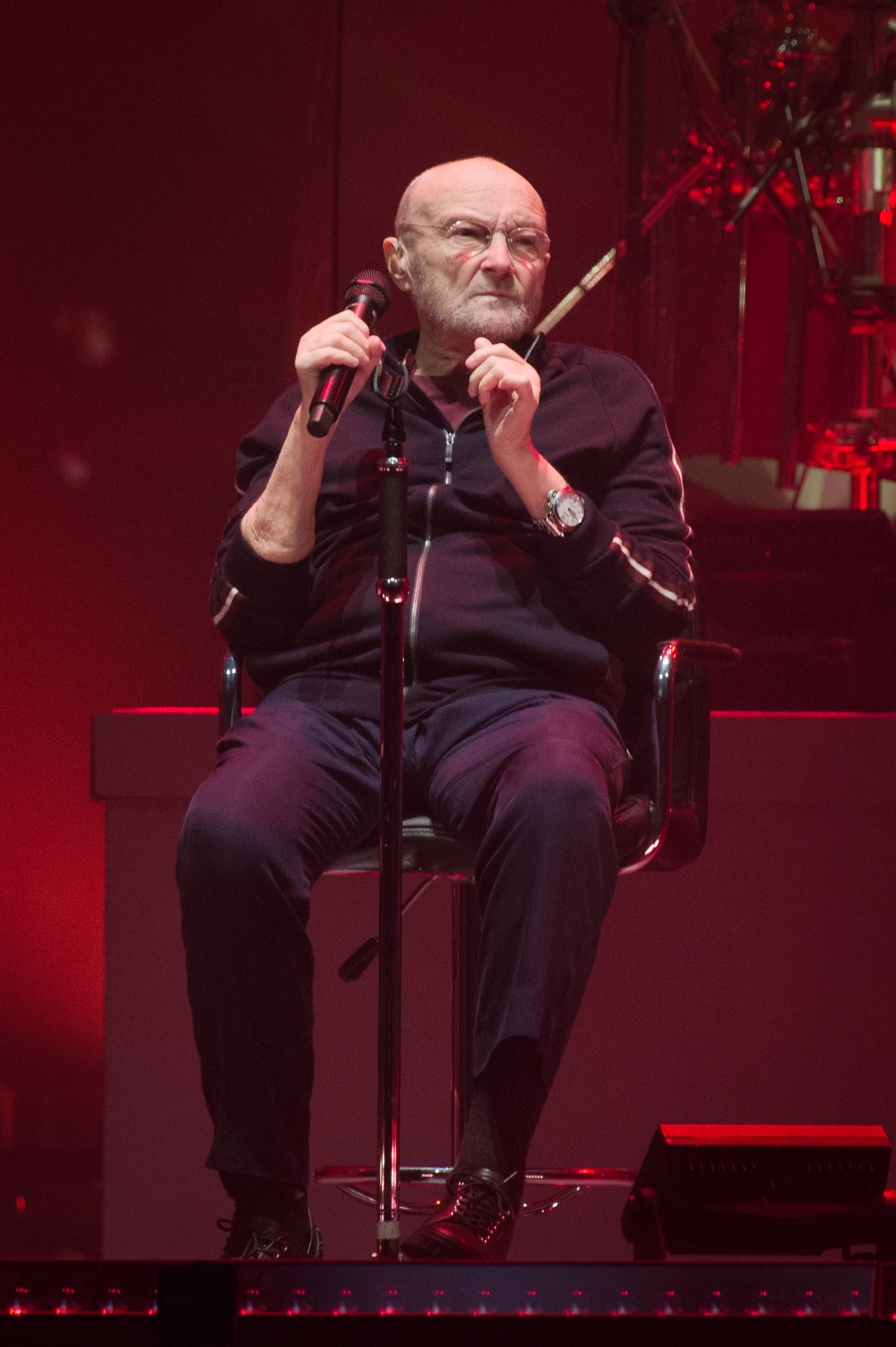 Phil Collins sitting on a chair as he sings onstage