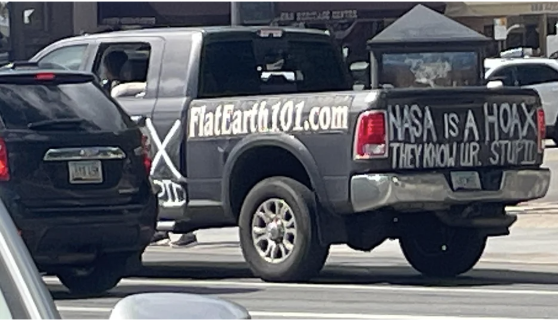 A truck with decals and writing that say &quot;Flat Earth 101 dot com&quot; and &quot;NASA is a hoax, they know you&#x27;re stupid&quot;