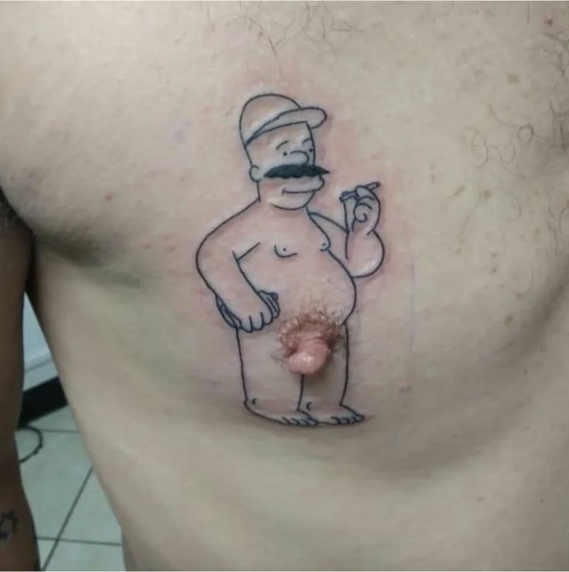 A cartoon character tattooed on a man&#x27;s chest so that his nipple has become the penis of the character