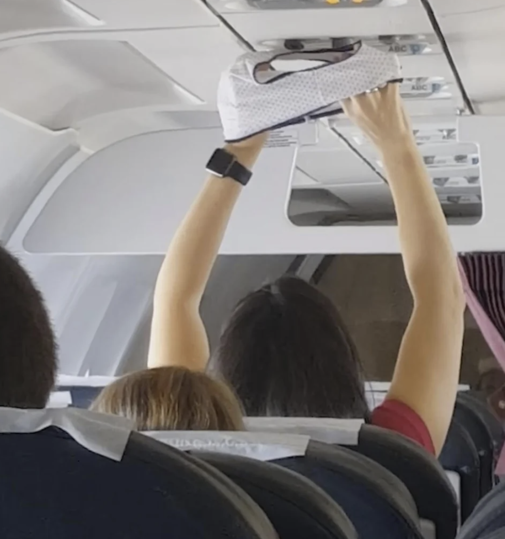 A woman on a packed plane is holding her underwear up to the overhead vent