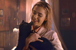 Kiernan Shipka holding Salem, a black cat, as Sabrina in Chilling Adventures of Sabrina