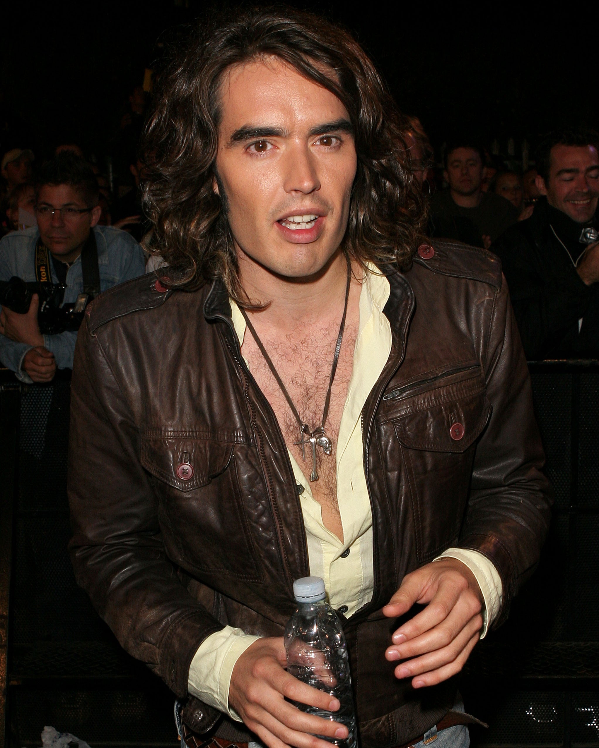 Closeup of Russell Brand at an event holding a bottle of water