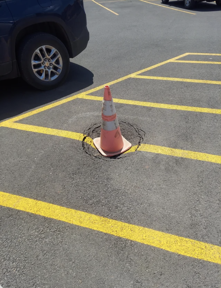 A traffic cone over a small crater on the road