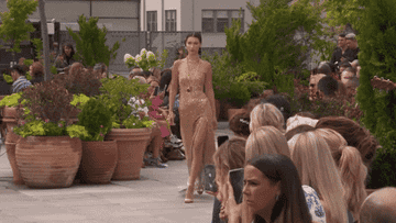 Bella Hadid walks down a runway wearing a shimmering gold dress.