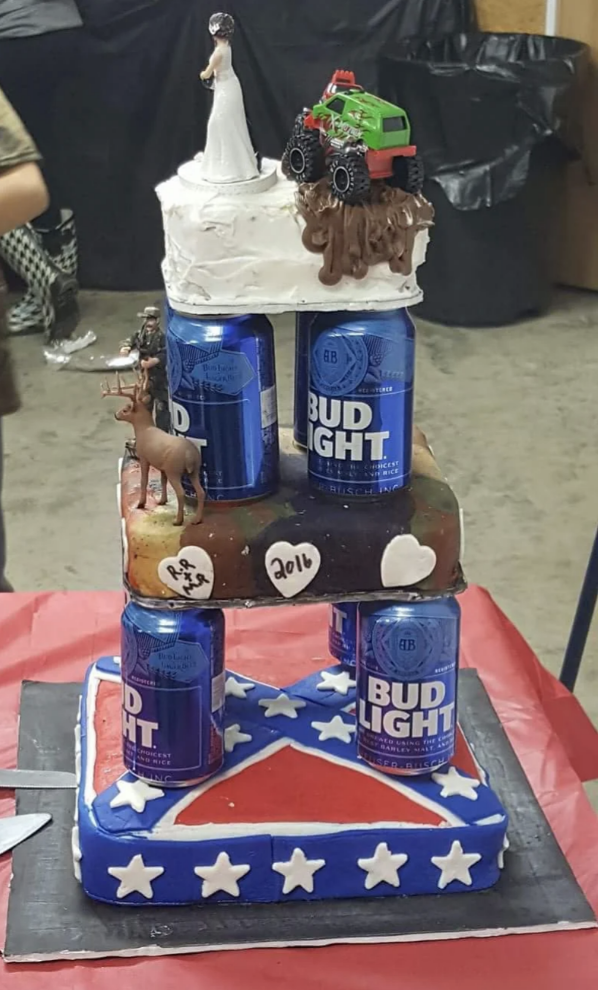 This cake has three tiers. The top tier has a monster truck, the middle tier shows a hunter shooting a deer, and the bottom tier is the Confederate flag