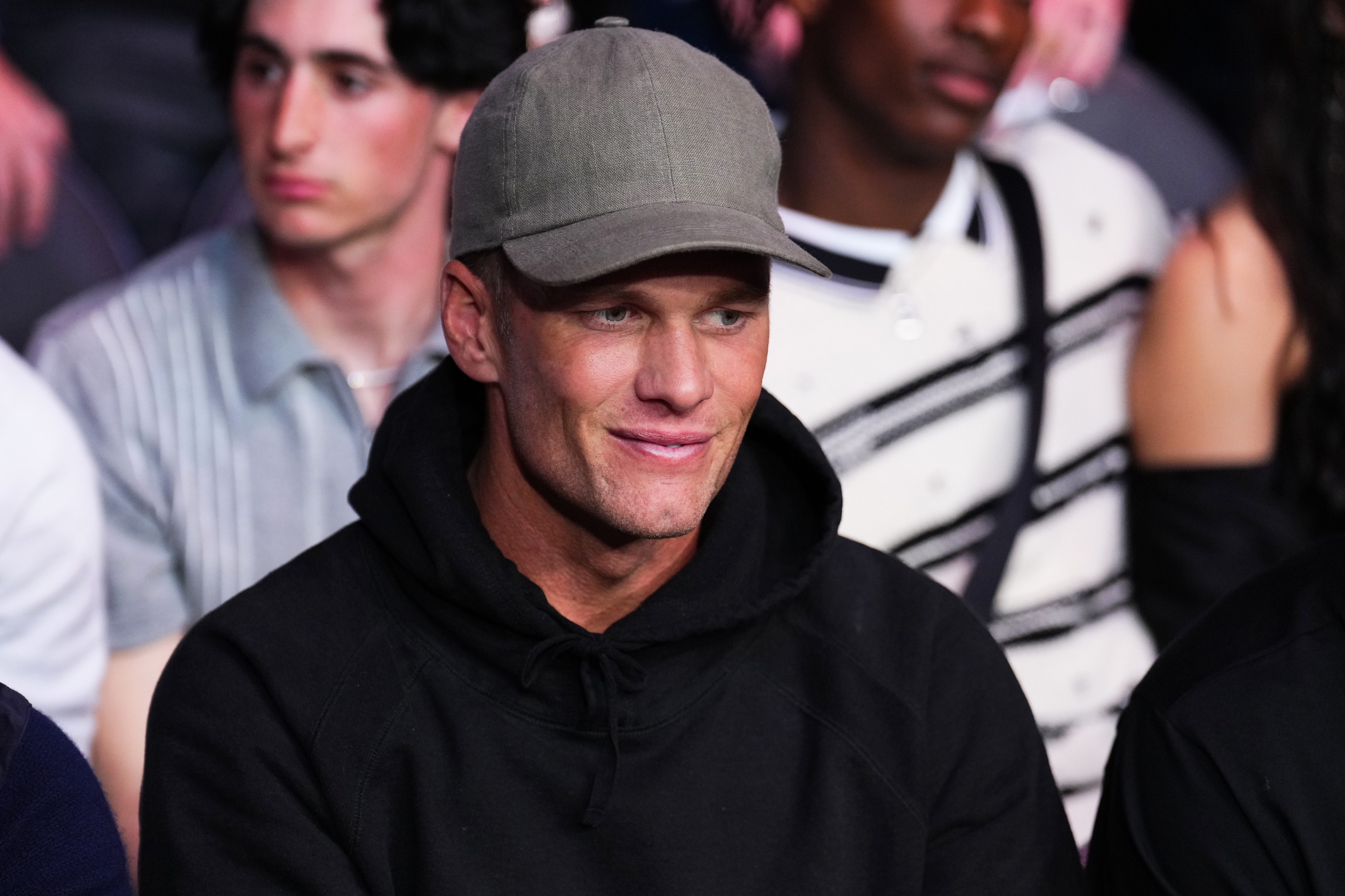 A closeup of Tom Brady wearing a baseball cap and a hoodie