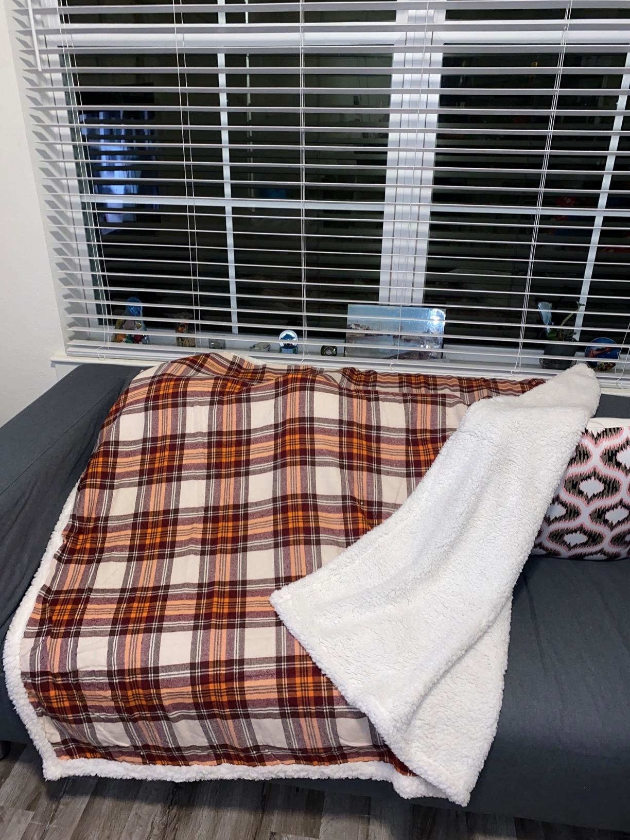 Reviewer image of the plaid blanket on their sofa, showing the soft sherpa side