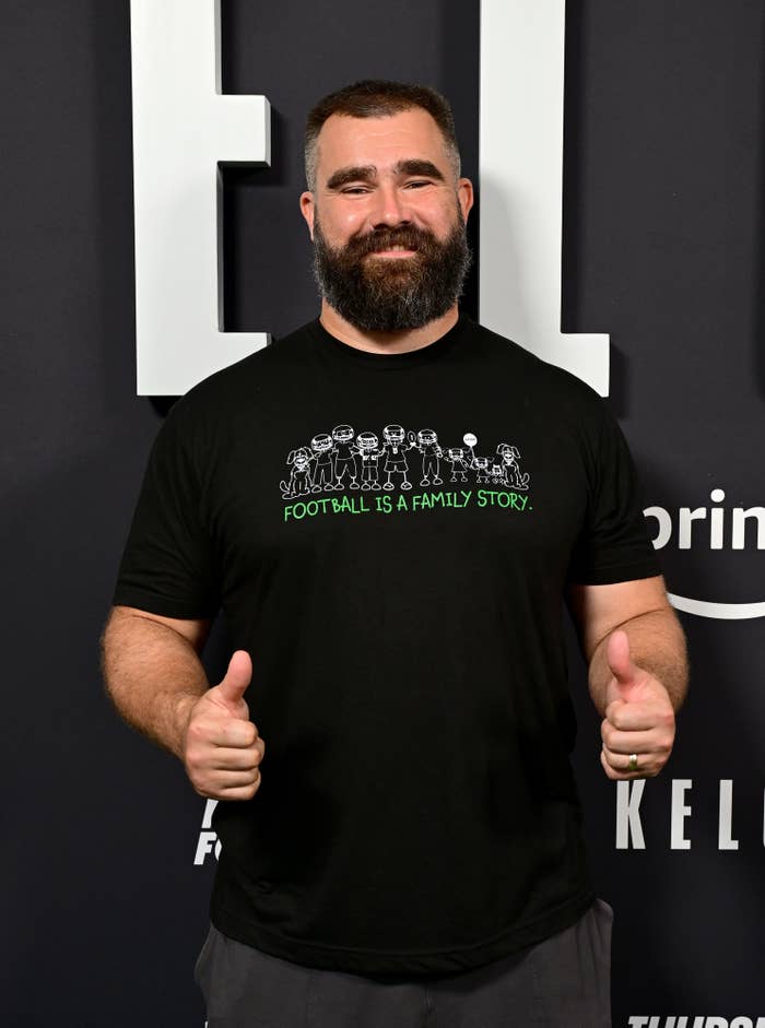 Closeup of Jason Kelce on the red carpet wearing a t-shirt that says &quot;Football is a famiily store&quot; and giving two thumbs up
