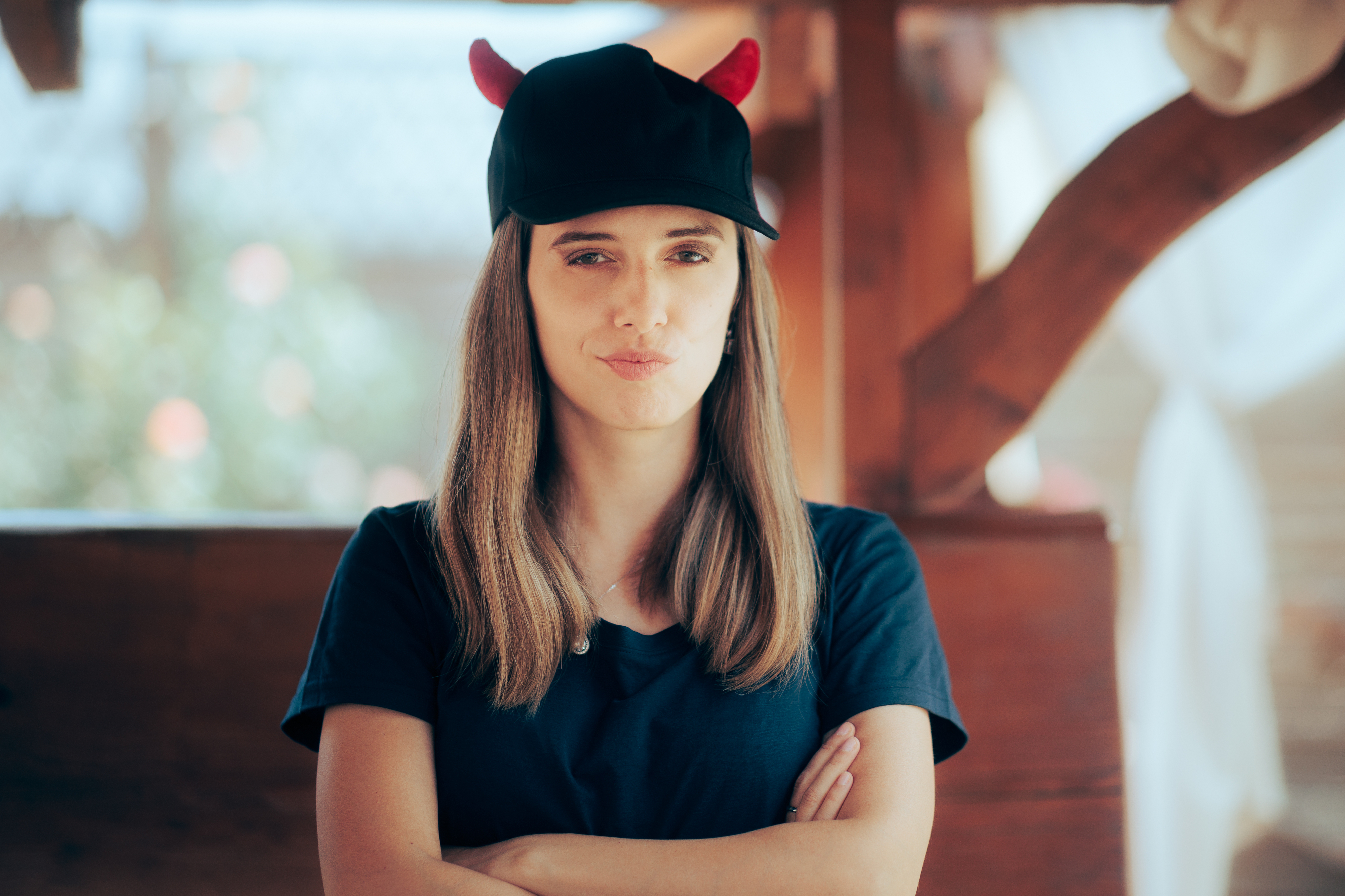 A woman with a hat that has devil horns and her arms crossed