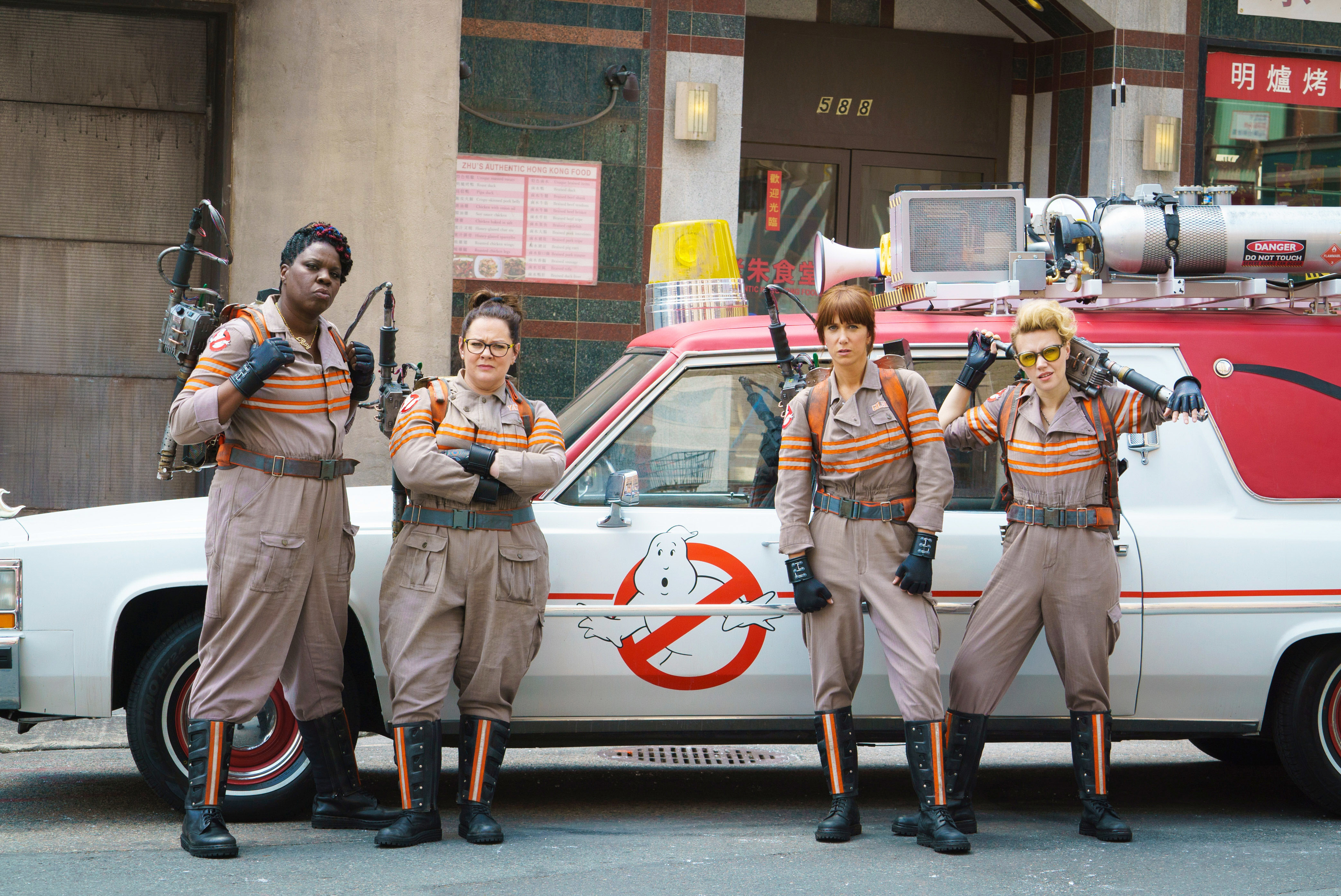 The cast of &quot;Ghostbusters&quot; standing fully suited up in front of their vehicle