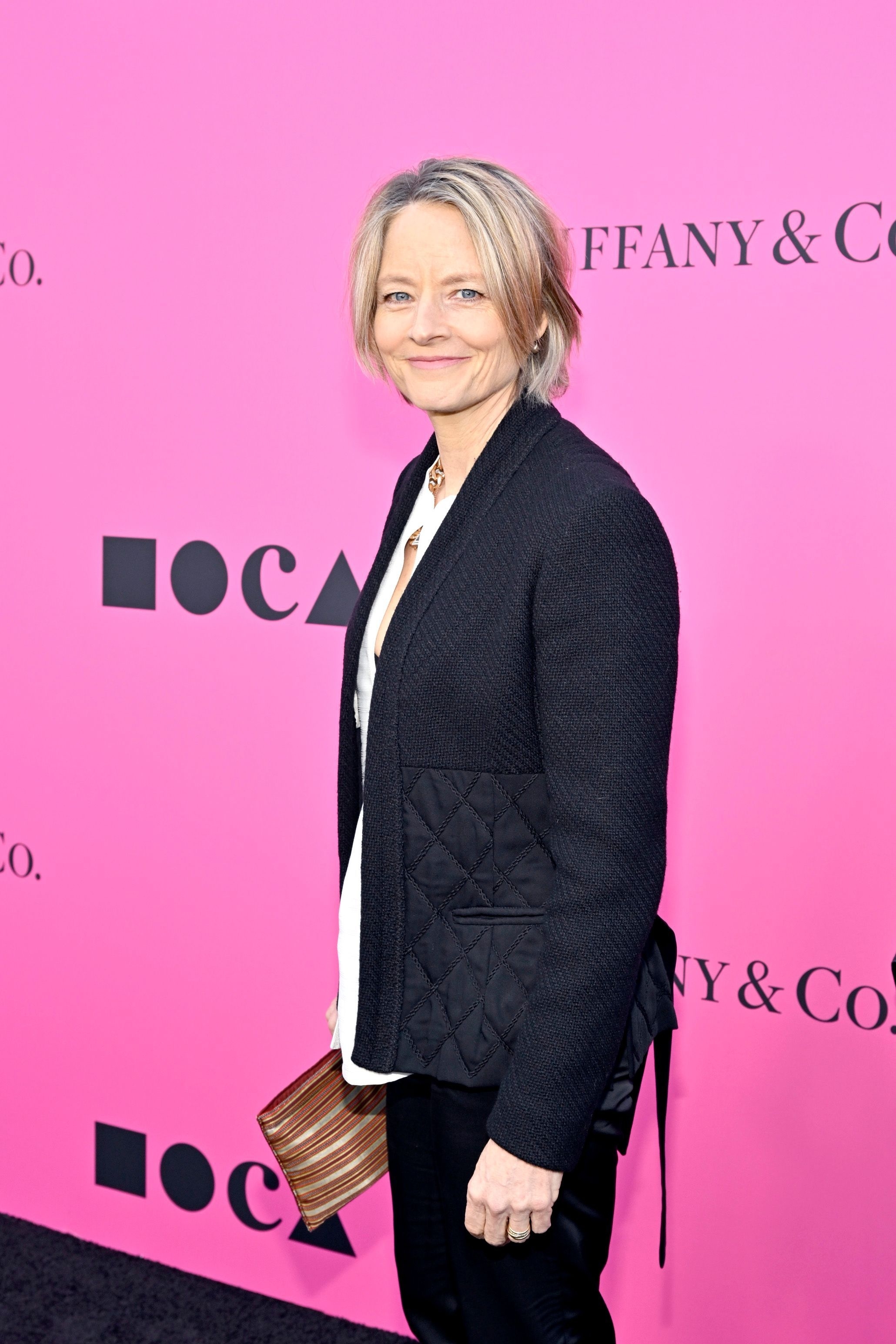 Close-up of Jodie smiling in a jacket and pants at a media event